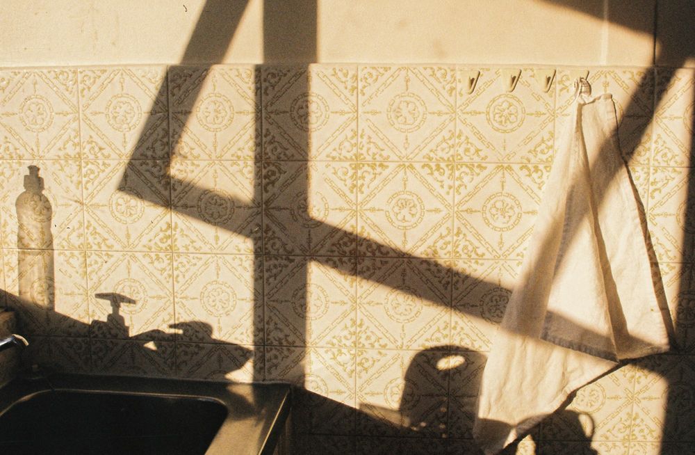 Morning sun throws the shadow of a window frame across a patterned tile wall behind a kitchen counter.