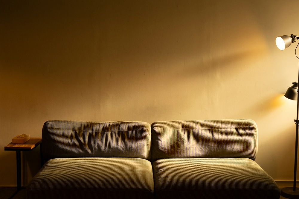 A low olive corduroy sofa against a warm wall, lit from the side by a standing lamp in the evening.