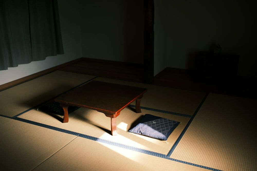 A dark tatami room late at night: a low table and a floor cushion in one pool of light.