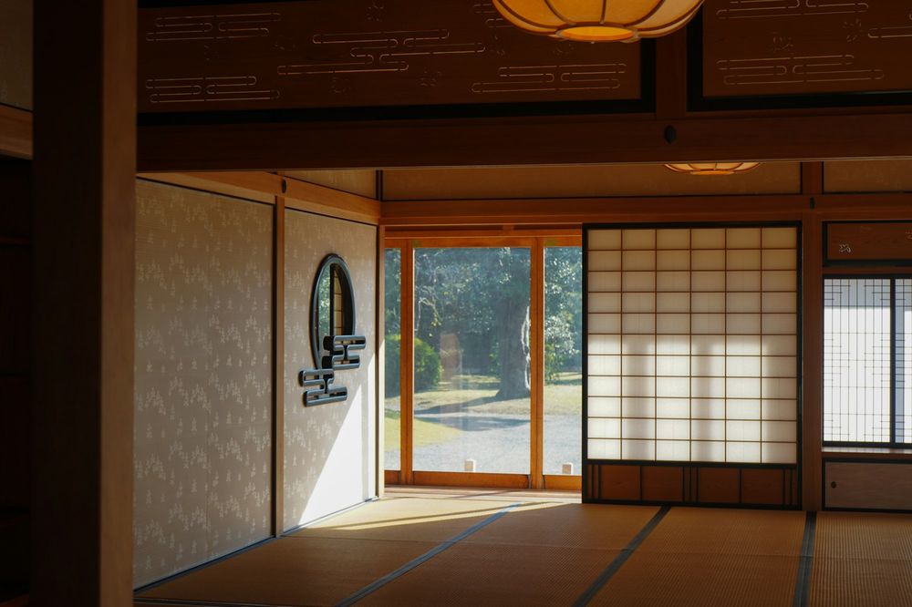 A tatami room with a round window and a glass door open to a garden, in soft daylight.