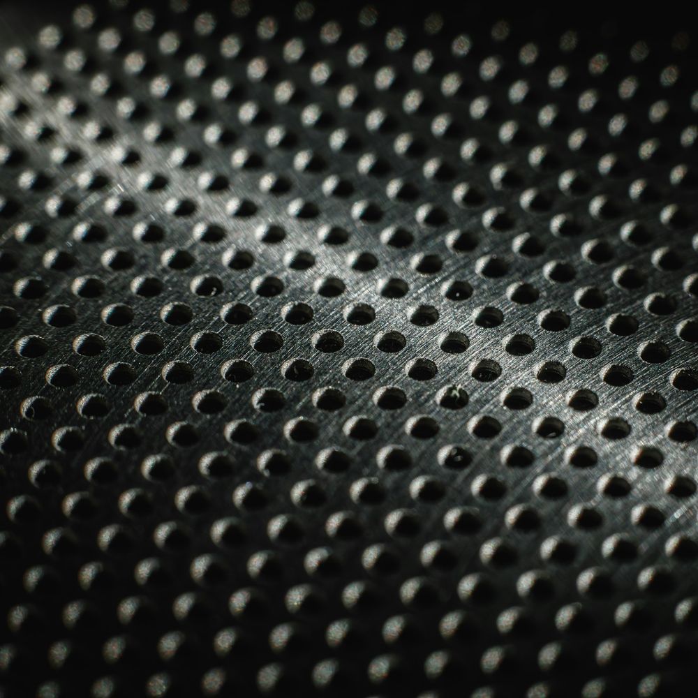 Dark perforated metal sheet with raised dimples catching a grazing light.