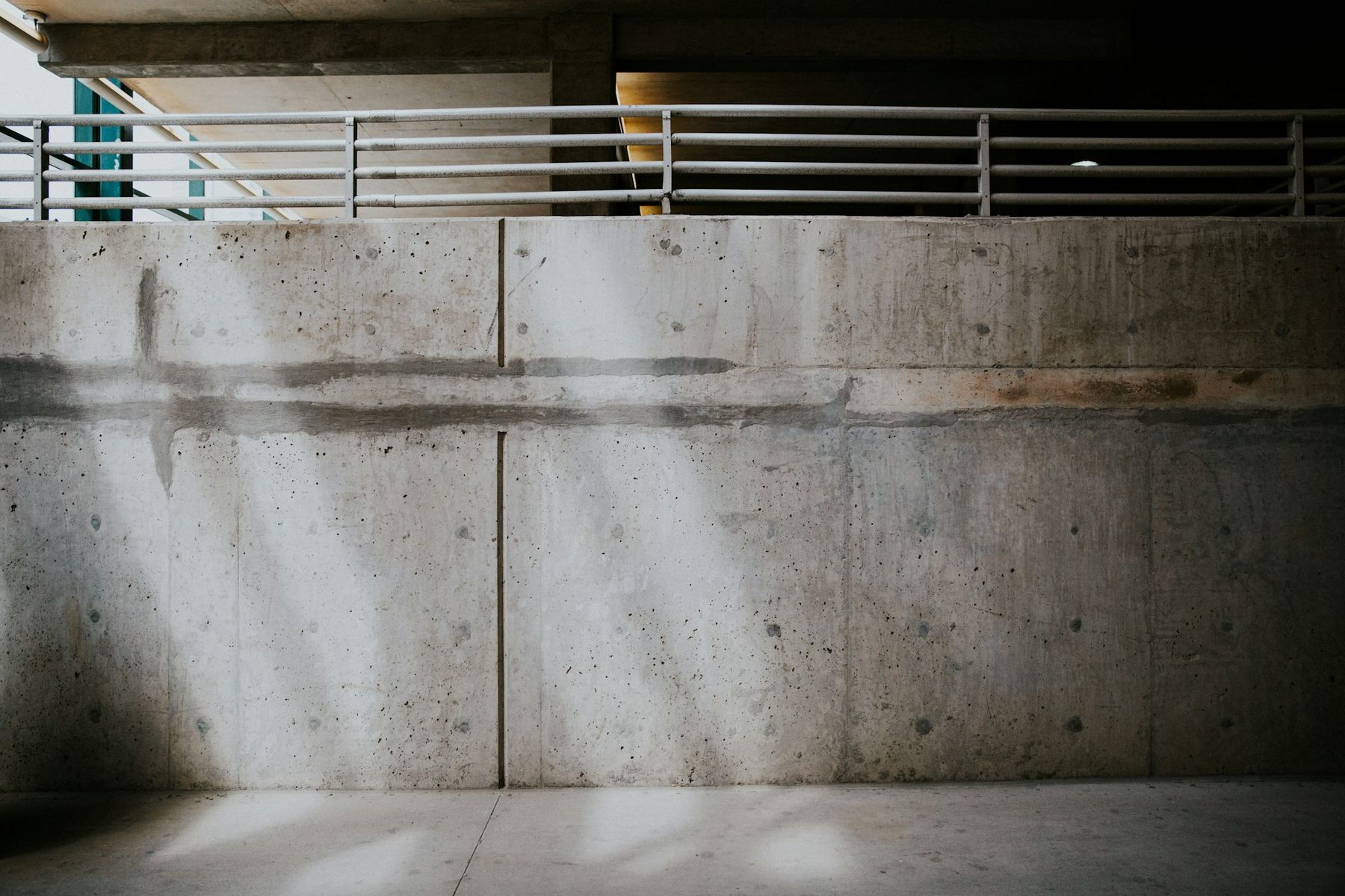 A board-formed concrete wall crossed by shafts of low sunlight, a steel railing along the top.