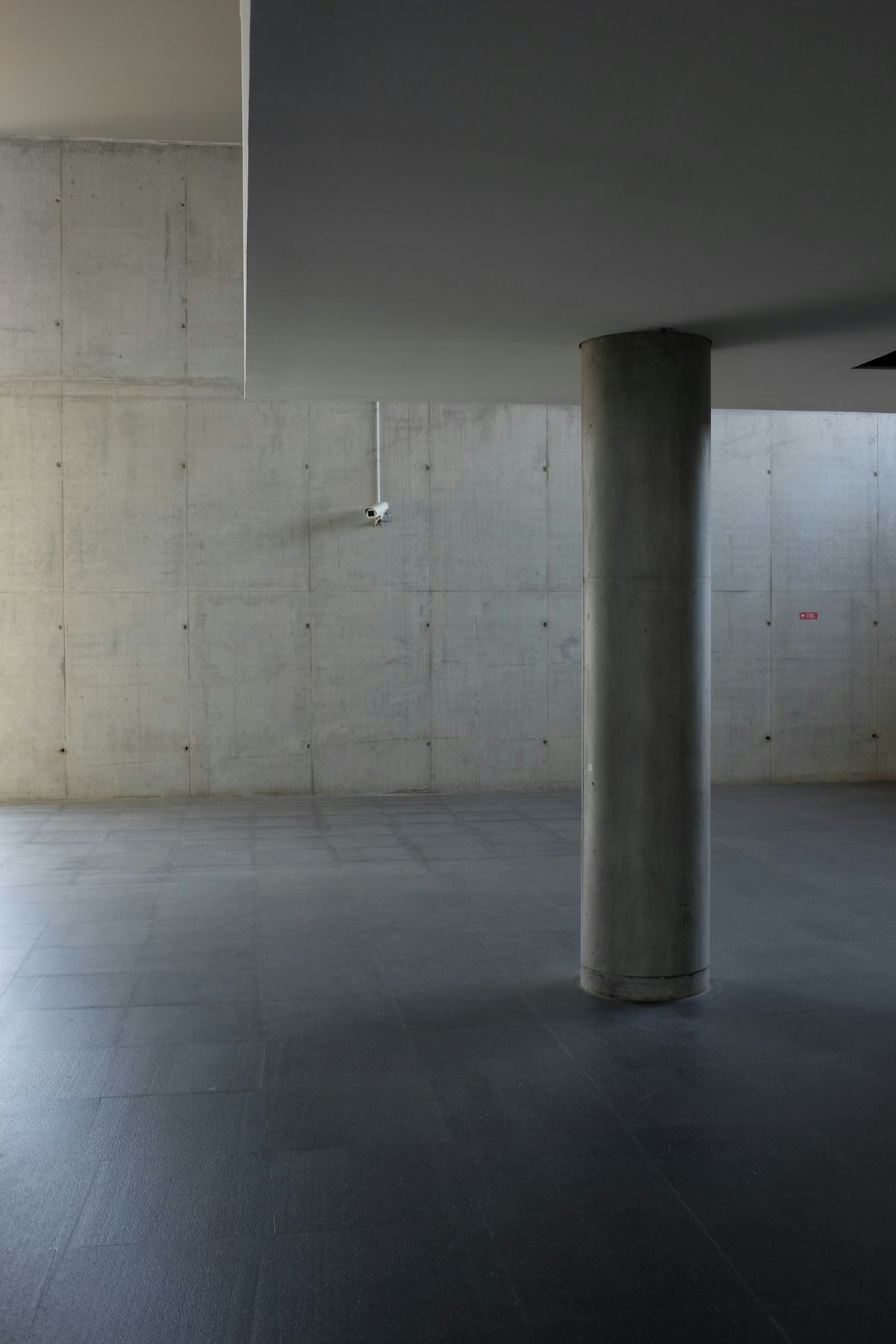 A single round concrete column in an empty grey hall, a pale wall behind.