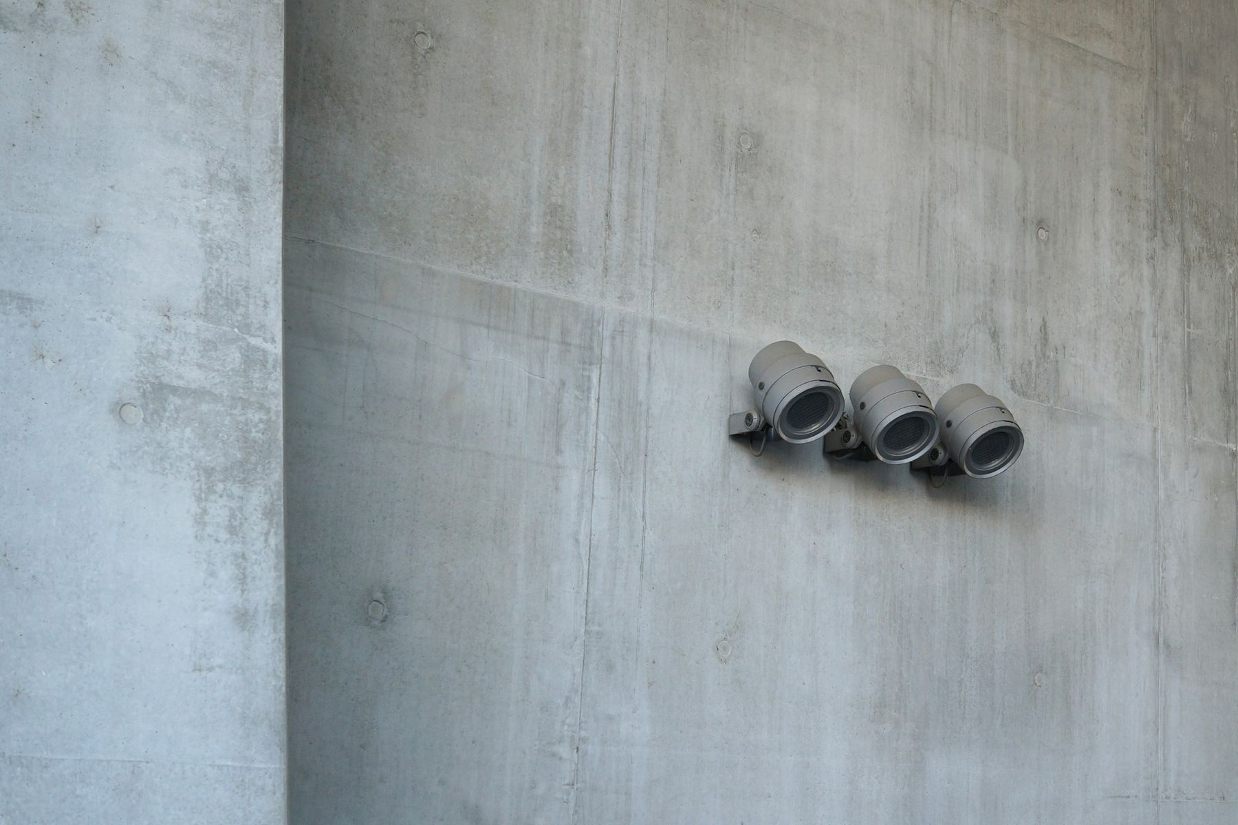 Three cylindrical fittings bolted to the face of a bare concrete wall.
