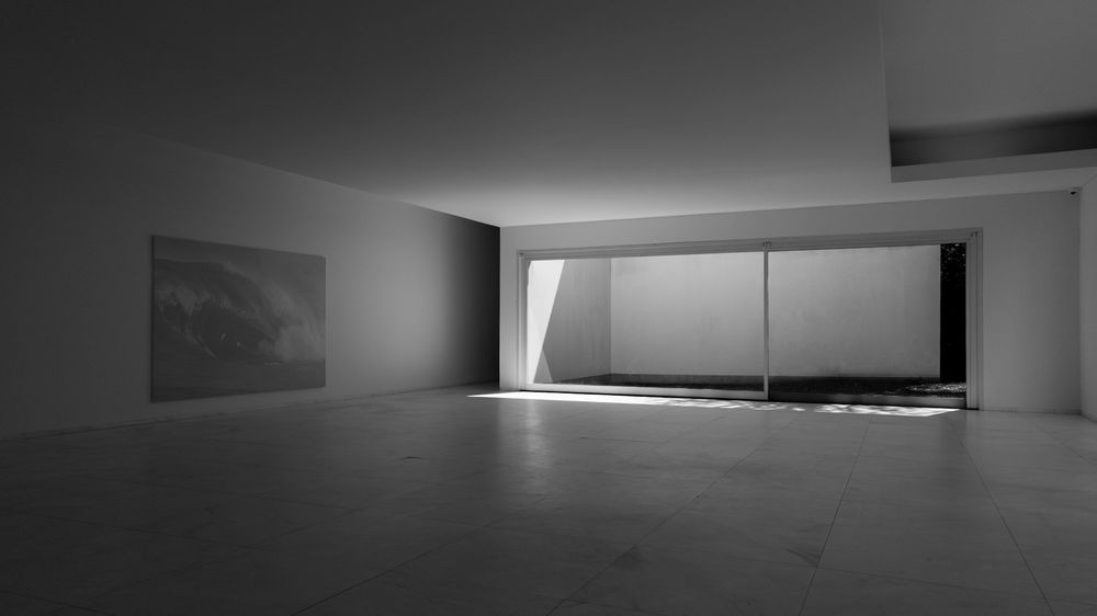 A dim, empty gallery. Grey daylight comes through a wide window and lies across a stone floor.