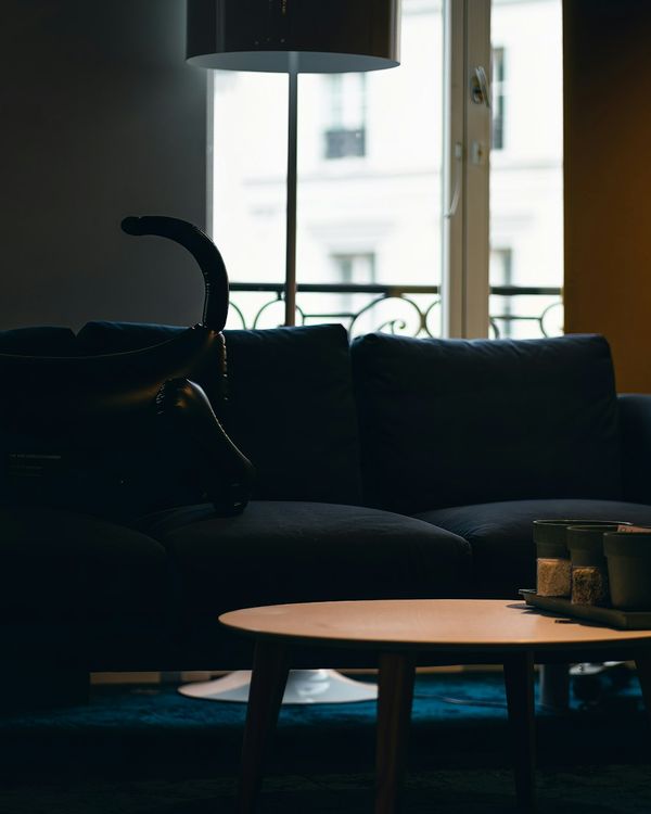 A dim living room with a dark sofa, a round wooden table and a tall window behind.