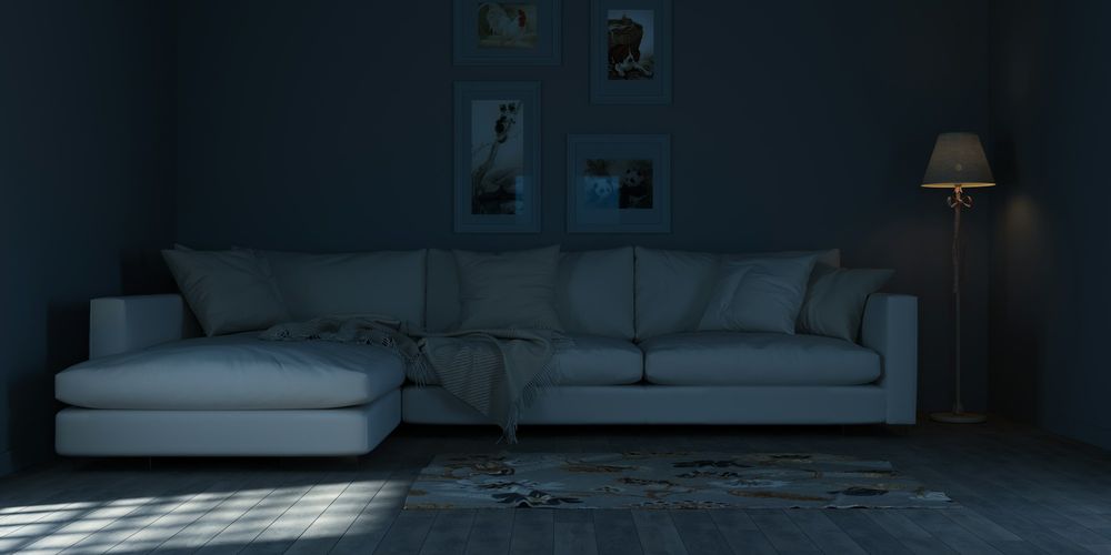 A living room at night, lit only by one floor lamp, with a white sofa against a dark wall.