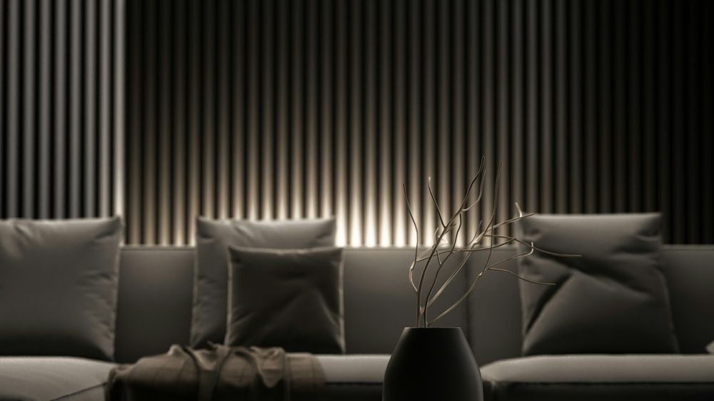 A dark lounge with a slatted wall lit from above, a grey sofa and a low stone table.