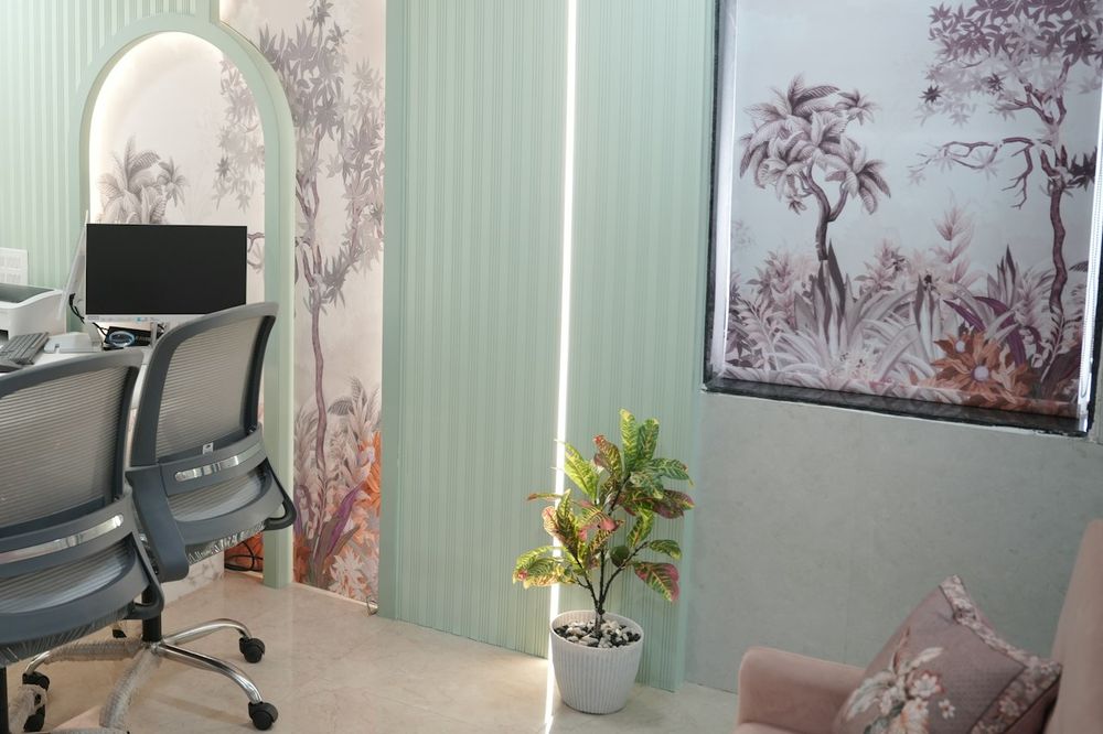 Pale green consulting room with a desk, two chairs and a botanical window blind