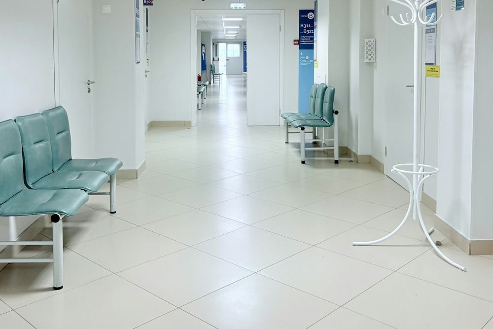 Bright clinic corridor with teal waiting chairs and a white coat stand