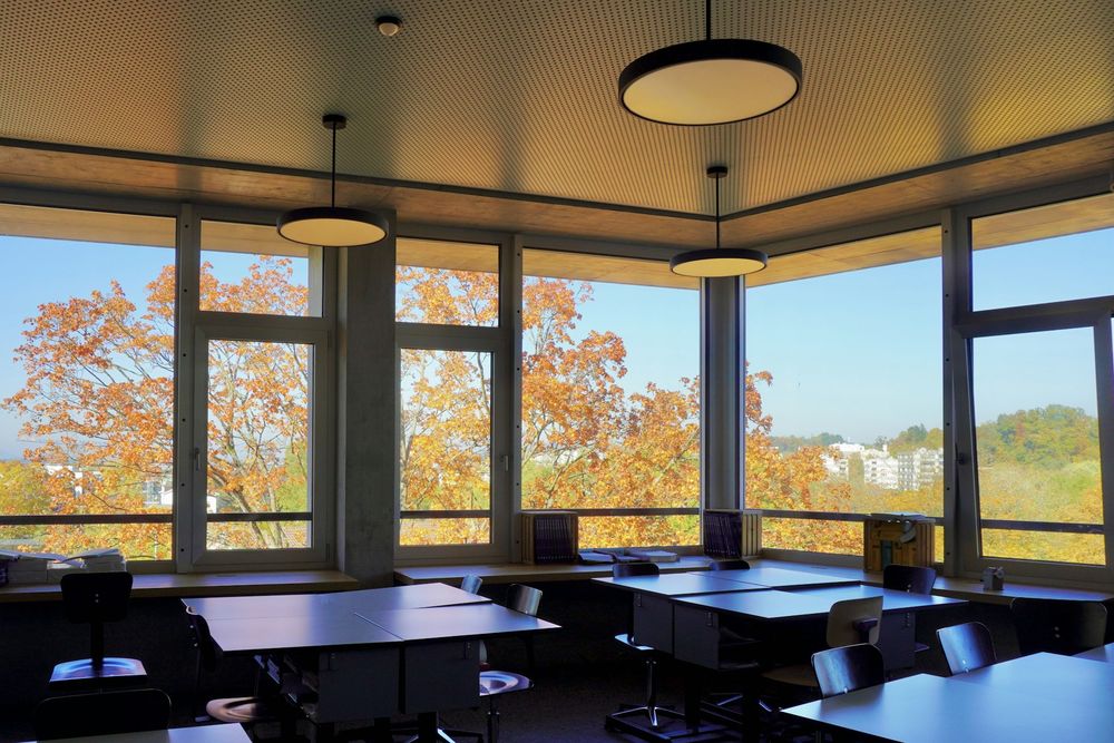 Classroom with desks and a corner of large windows onto autumn trees