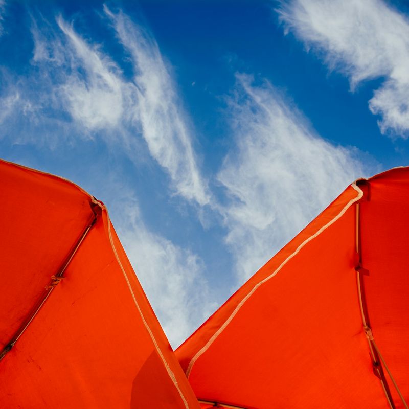 Two red parasols against a bright blue summer sky.