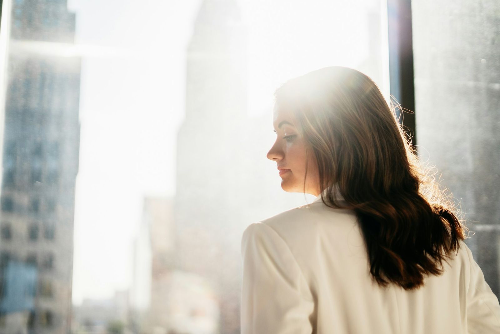 A woman turning away from strong, hazy summer sunlight between city towers.