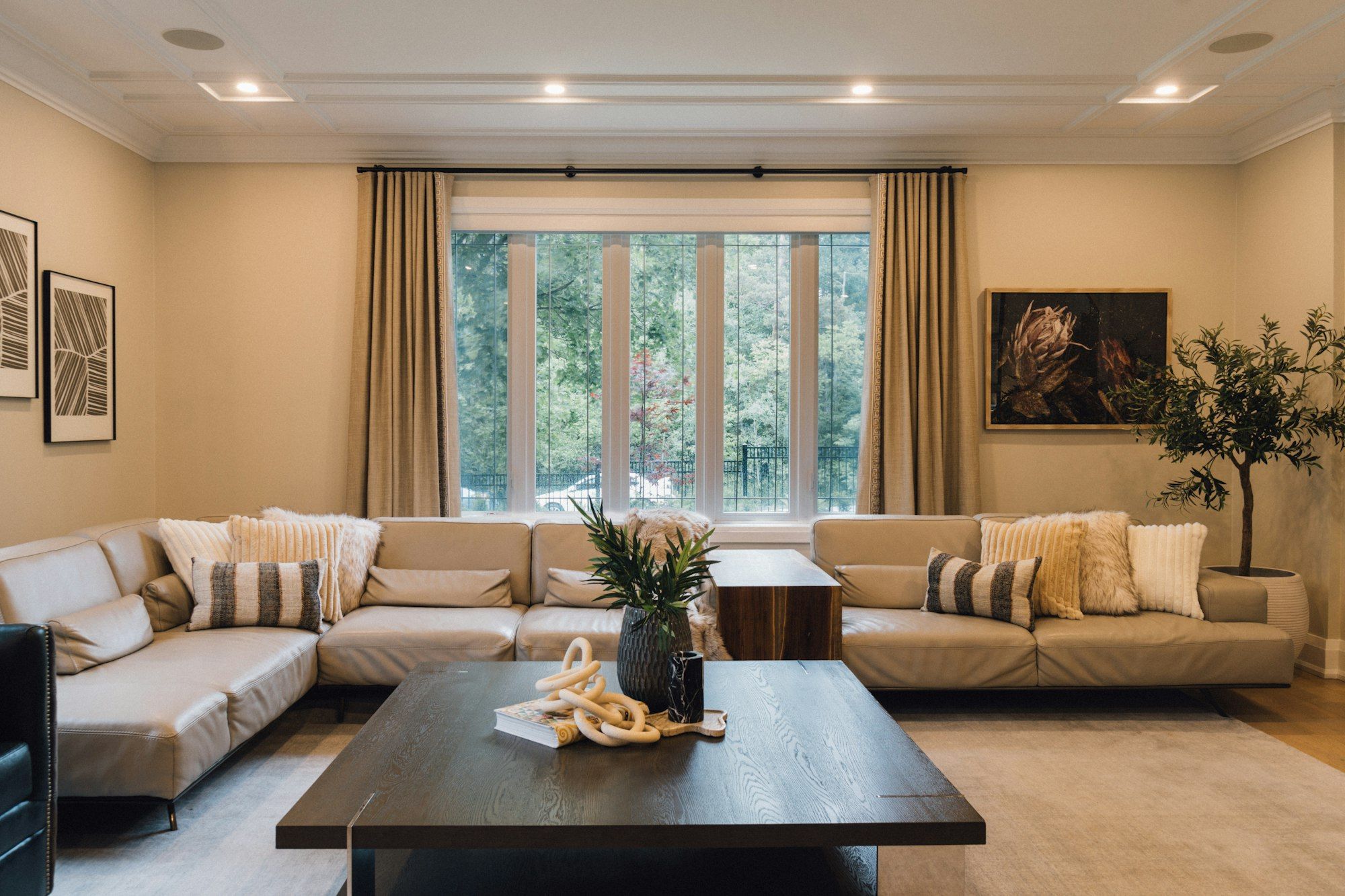 A living room with a long corner sofa facing a tall window with curtains