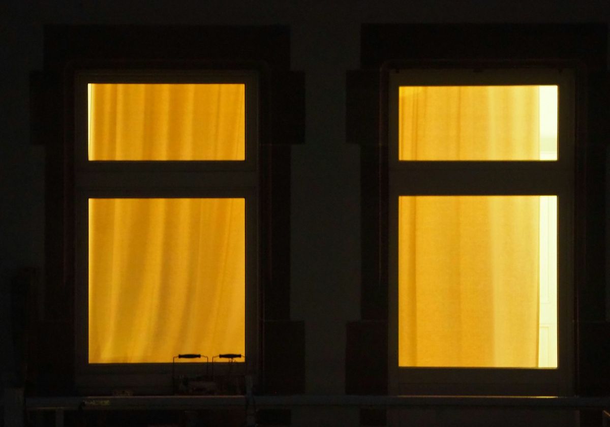 Two windows across the street at night, lit from inside behind yellow curtains.