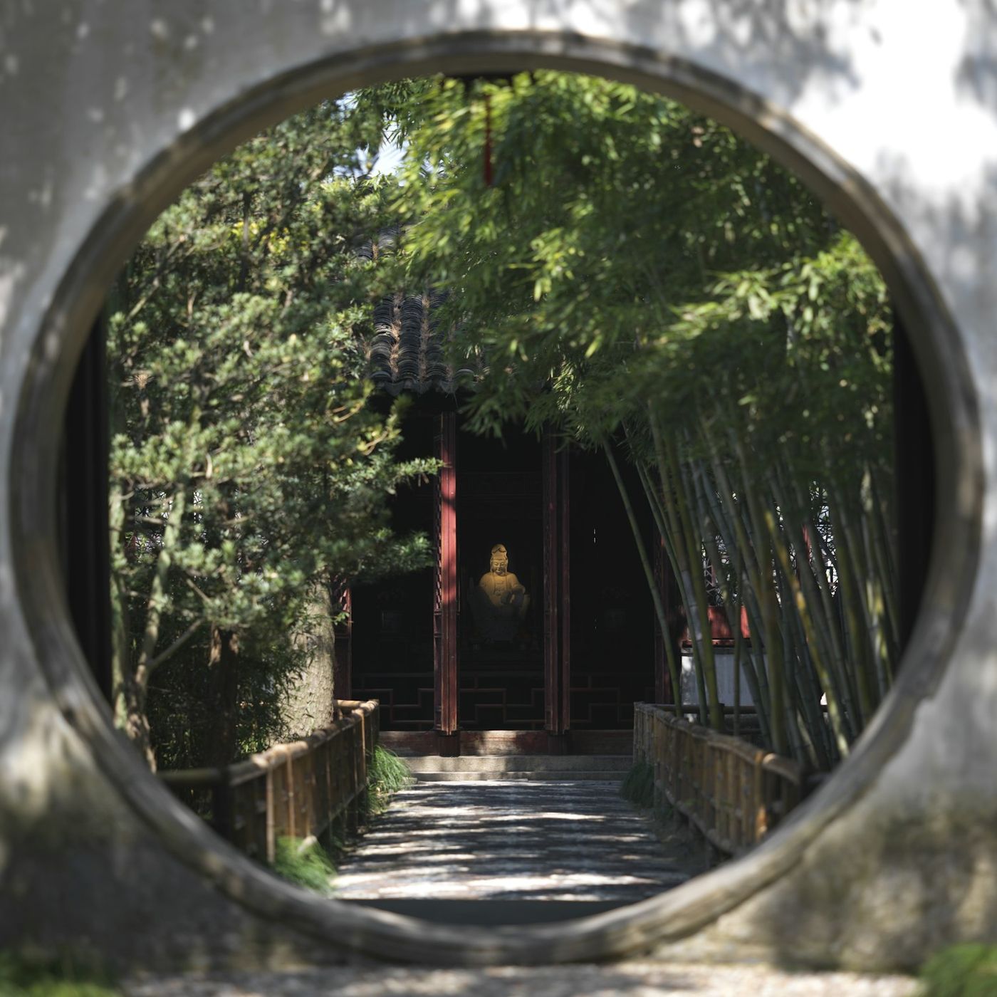 A round moon gate in a white wall, opening onto a bamboo path