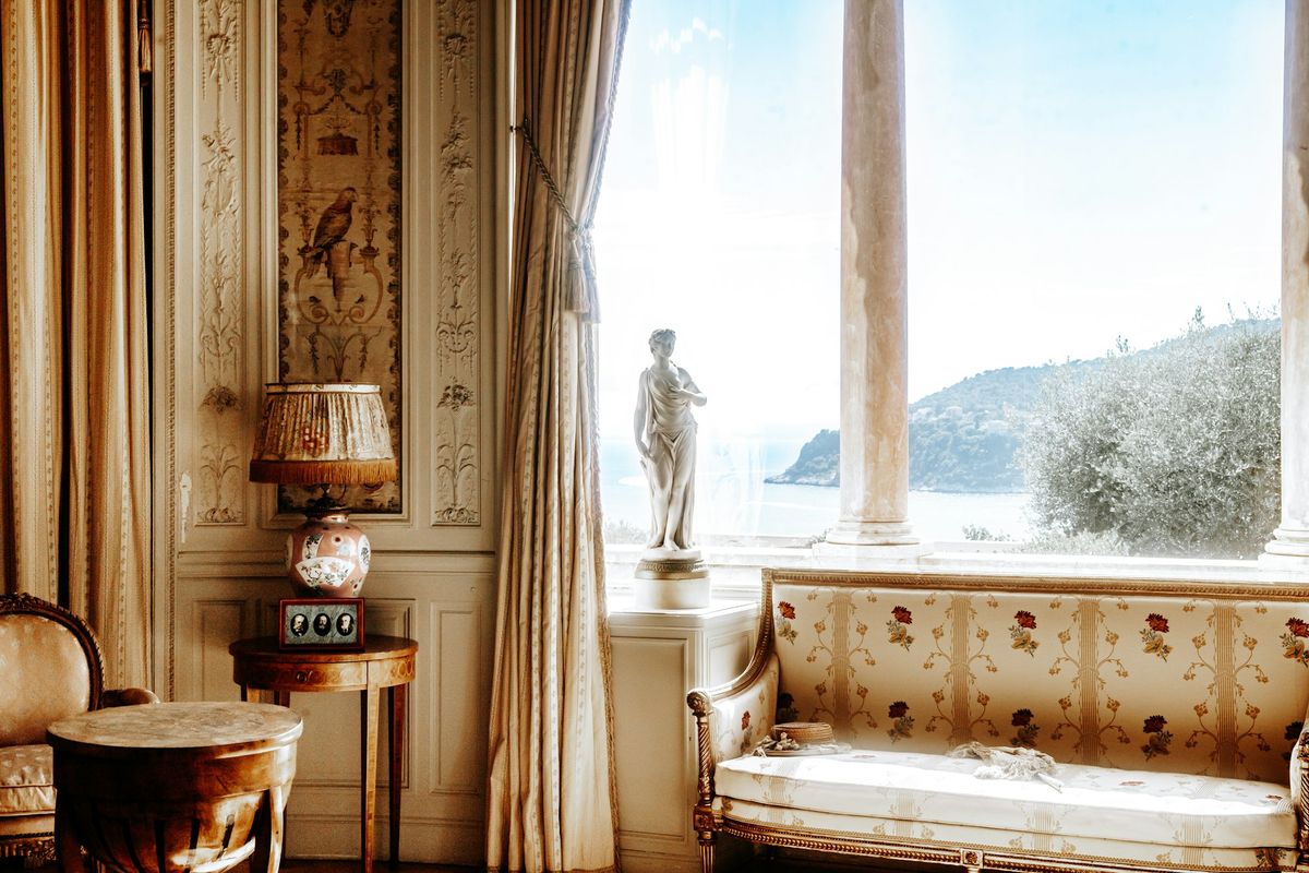 A classical drawing room with painted panelling, a marble statue in the window and the sea beyond.