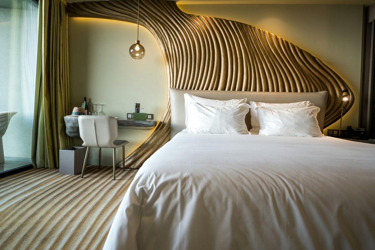 A bedroom with a sculpted wooden headboard that curves up the wall, lit from behind, and a white bed.
