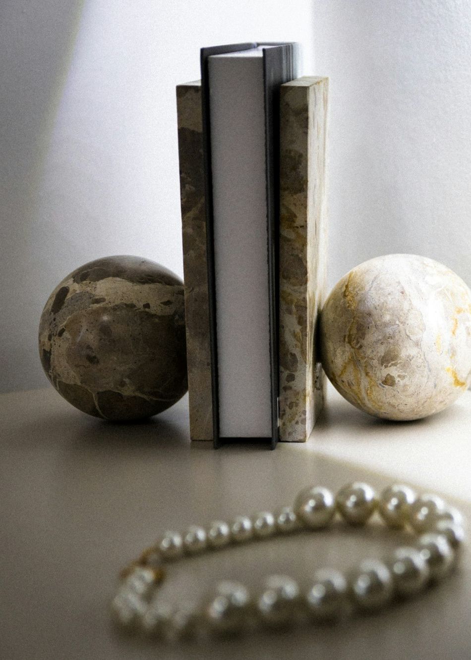 Two marble spheres and a pair of books on a pale shelf, a string of pearls in the foreground.