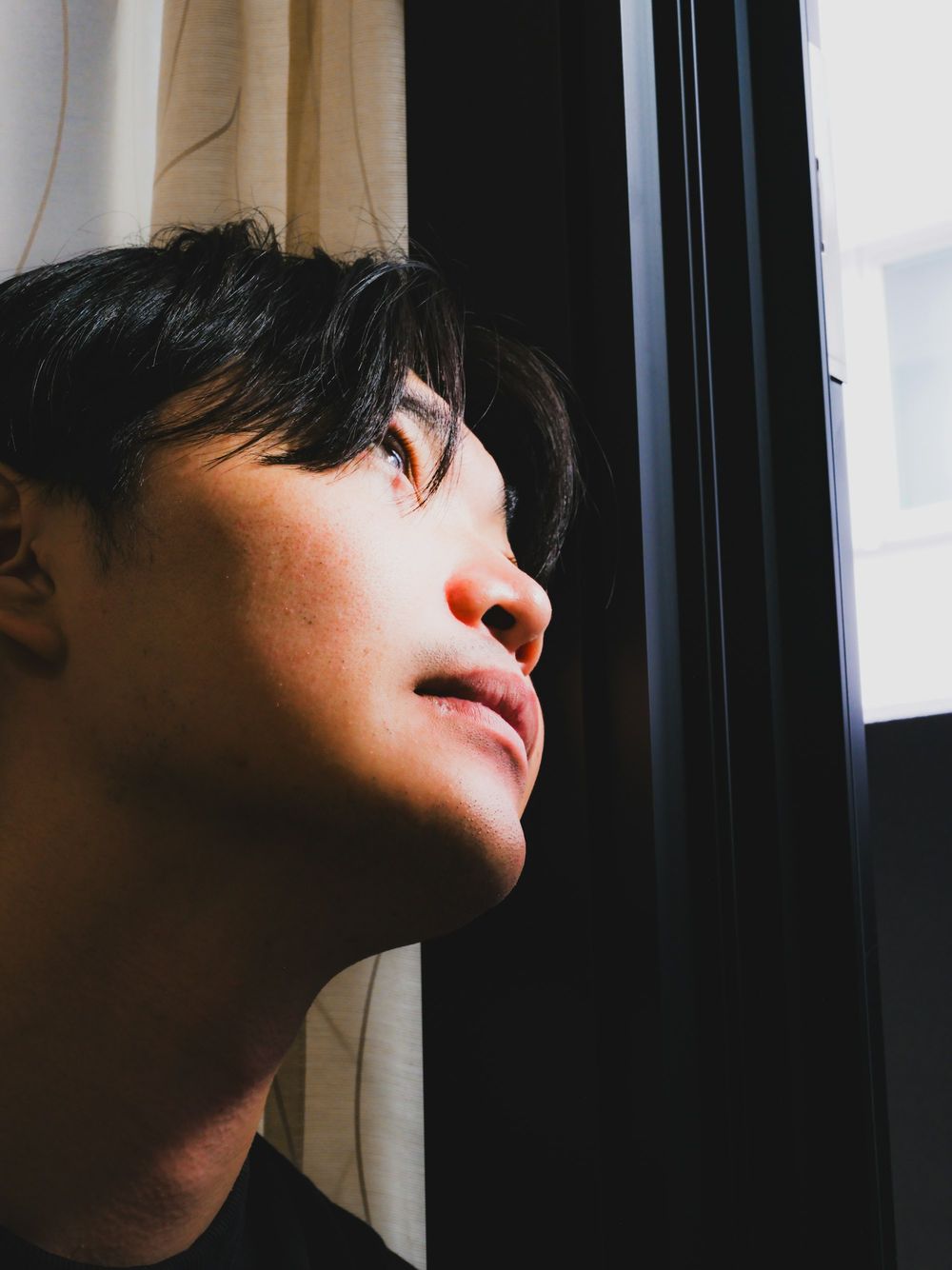 Close-up of a young man's face turned up towards window light.