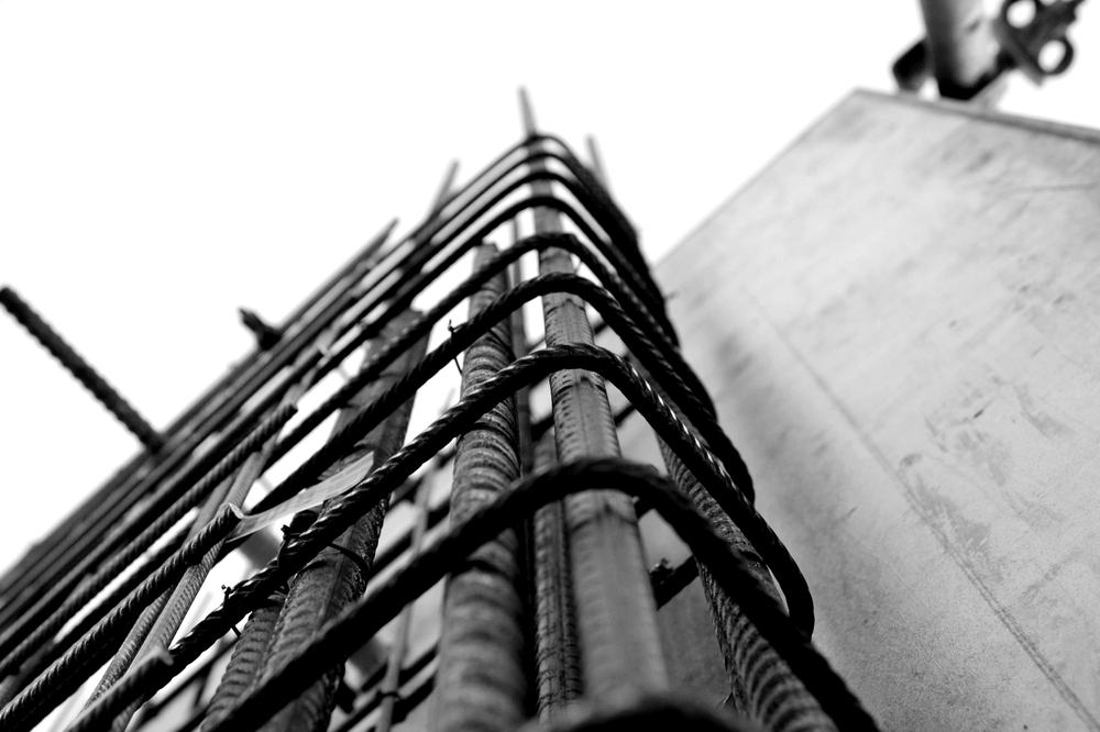 Close-up of a rebar cage rising against a concrete wall.