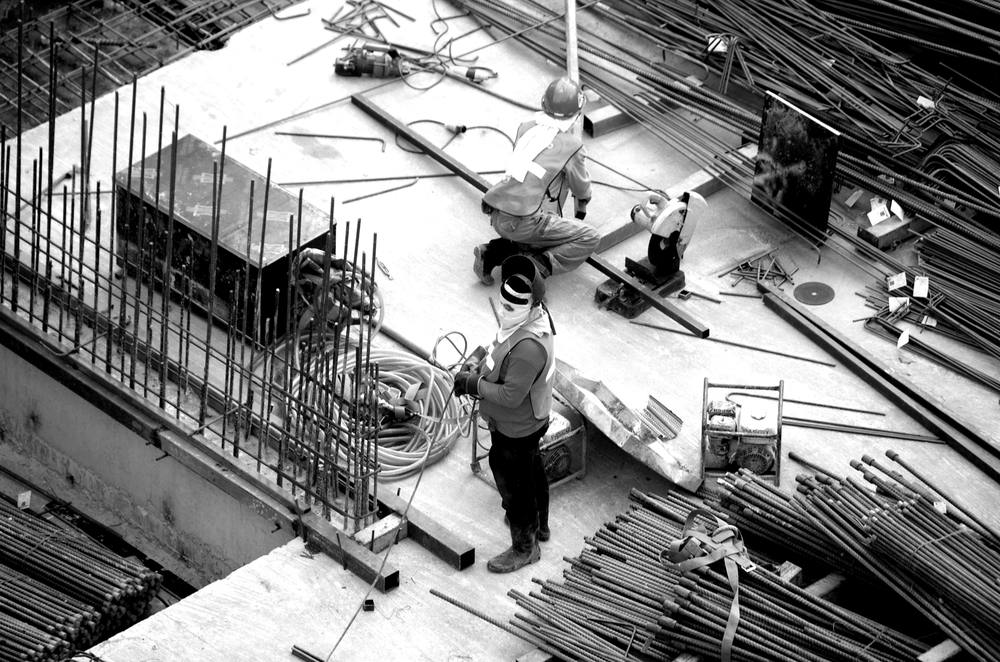 Two workers on a rebar deck among bundles of steel bars and hoses, seen from above.