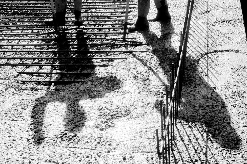 Shadows of two workers falling across rebar and fresh concrete.