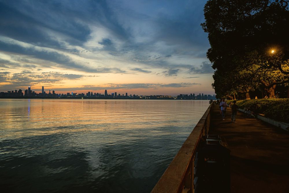 Sunset over the river, seen from a tree-lined promenade on the bank.