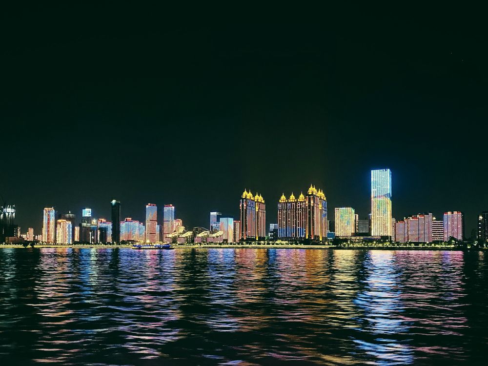 The Wuhan riverfront at night, lit towers reflected in the water.
