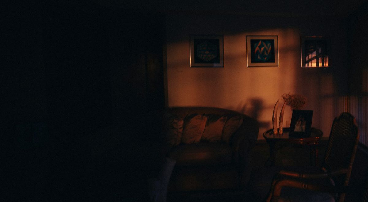 A dark sitting room; late sun falls on the far wall above a sofa and a small table.